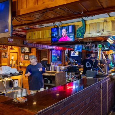 Two bartenders working behind a rustic wooden bar with TVs overhead.
