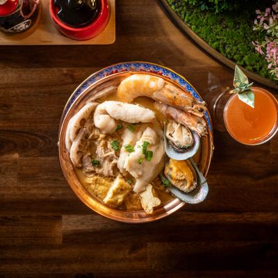 Szechuan hot pot served on a table with an orange drink.