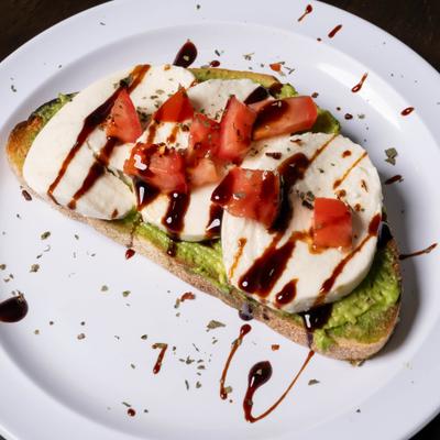 Caprese avocado toast with mozzarella slices, tomatoes, and a balsamic glaze.