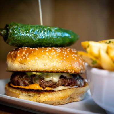 Cheeseburger on a seeded bun with a roasted jalapeno on top, served with fries.
