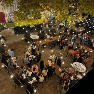 Evening courtyard scene with diners, string lights, and mural wall.