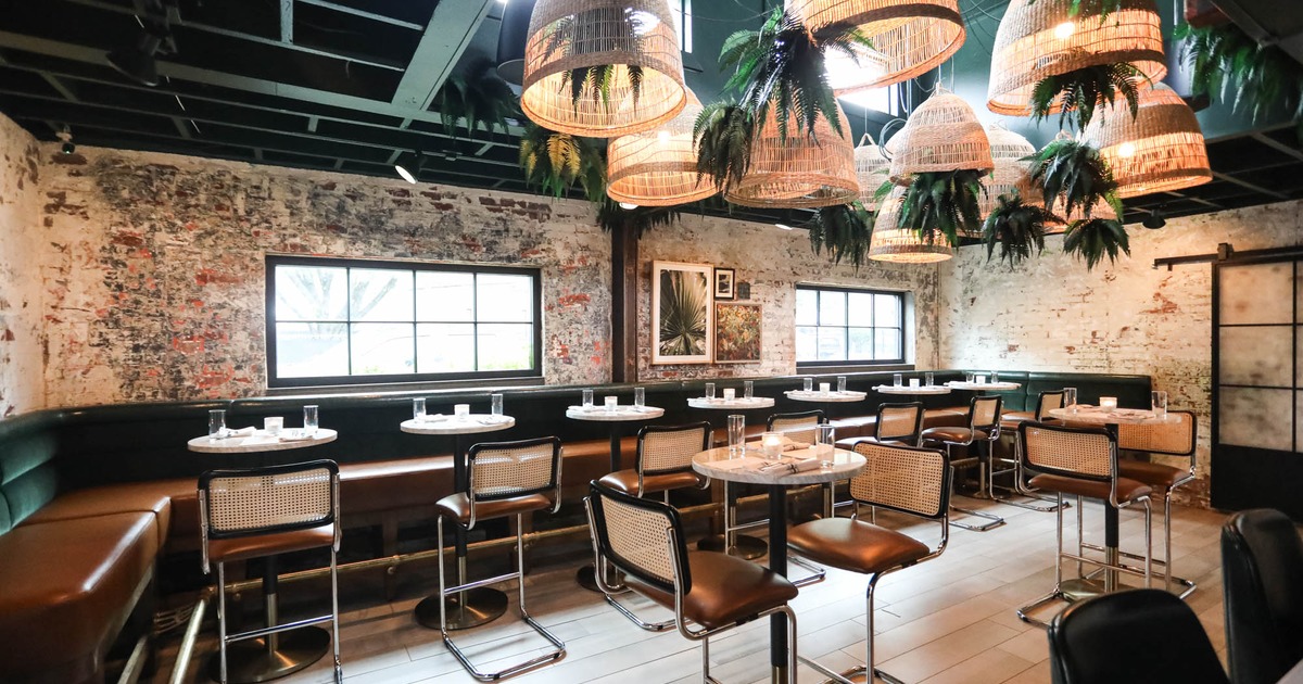 Green room, banquette seating and tables, rattan pending lights with greenery on the ceiling
