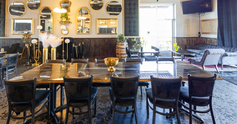 Interior, large polished table, black chairs, mirrors, potted plants, gray sofa