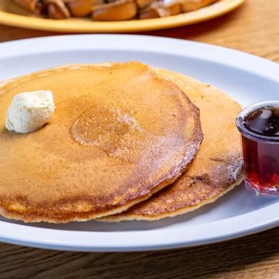 Two pancakes with butter and a cup of syrup.
