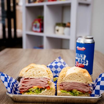 Ham sandwich with lettuce and tomato, served with a can of beer.
