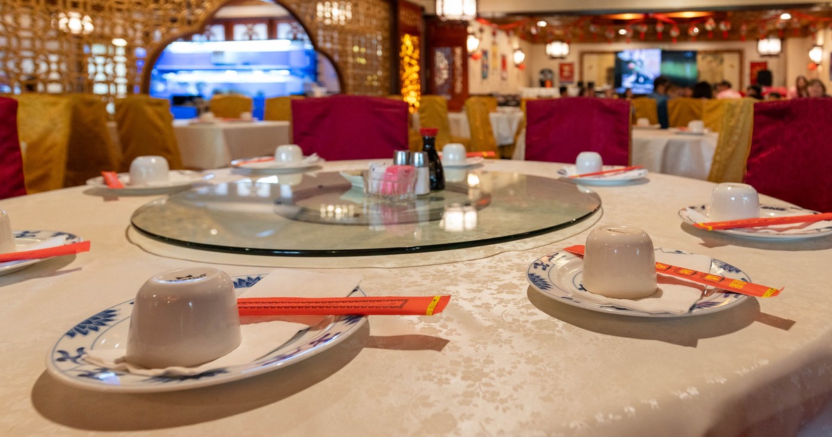 Circular table with white plates & red chopsticks, surrounded by brightly colored chairs.