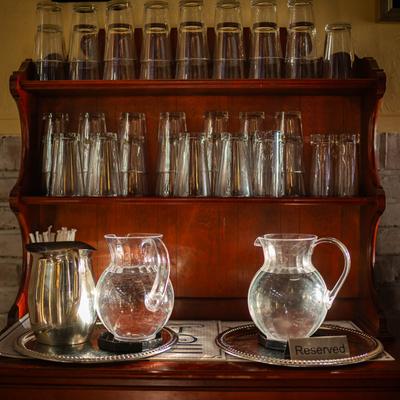 Interior, a wooden shelf displaying an assortment of glassware and water pitchers.