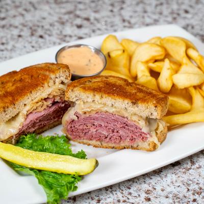 Reuben sandwich served with fries, dipping sauce, and a pickle spear.
