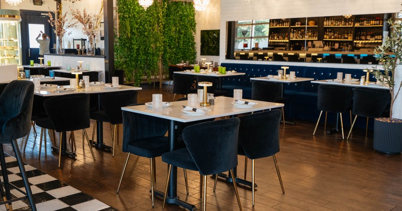 A modern restaurant interior with velvet chairs, white tables, chandeliers