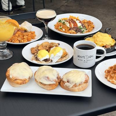 Various brunch dishes served on the table with cocktails and a cup of coffee.