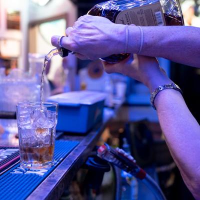 Bartender pouring an alcoholic beverage from a bottle into a glass filled with ice.