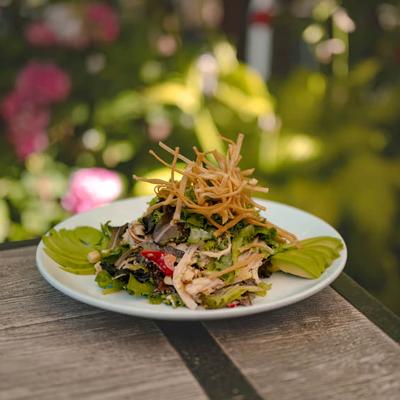 Salad with mixed greens, shredded chicken, sliced avocado and crispy topping.