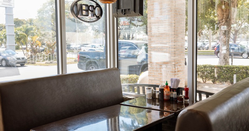 Booth with dark brown seats, a glossy table, overhead light and large windows.