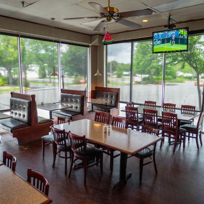 A casual restaurant dining room features wooden tables, booths, and large windows.