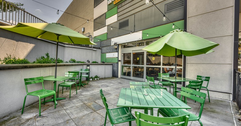 Outdoor patio with green tables and chairs under umbrellas at a restaurant entrance