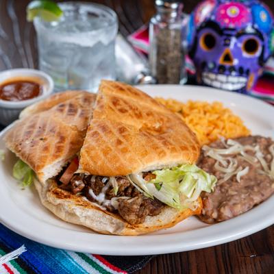 Mexican torta sandwich served with rice, refried beans, red salsa, and a drink.