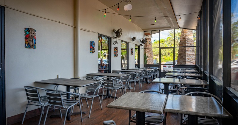 Outdoor dining area, metal tables and chairs, string lights, decorative masks and large windows