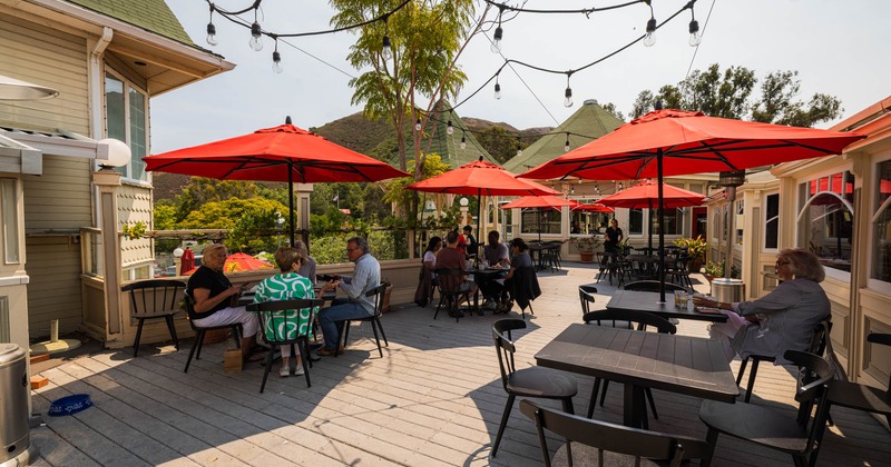 Outdoor patio with people seated at tables under bright red umbrellas