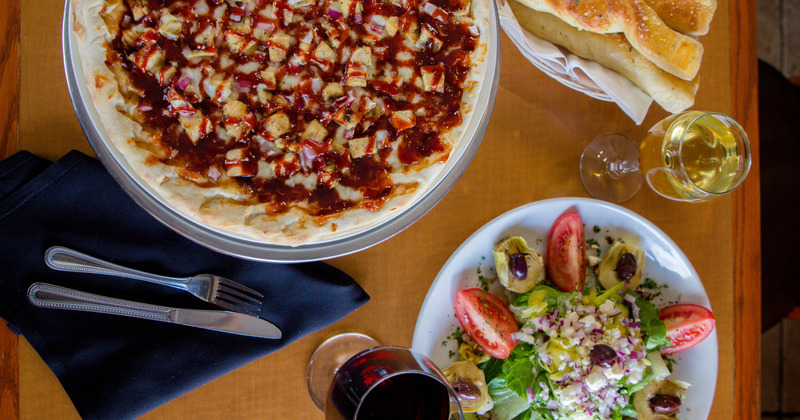 A pizza, salad bowl, wine and Italian bread, served on a table, top view