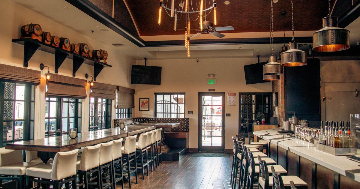 Interior view of a contemporary bar with a long wooden table, white stools, and a sleek bar