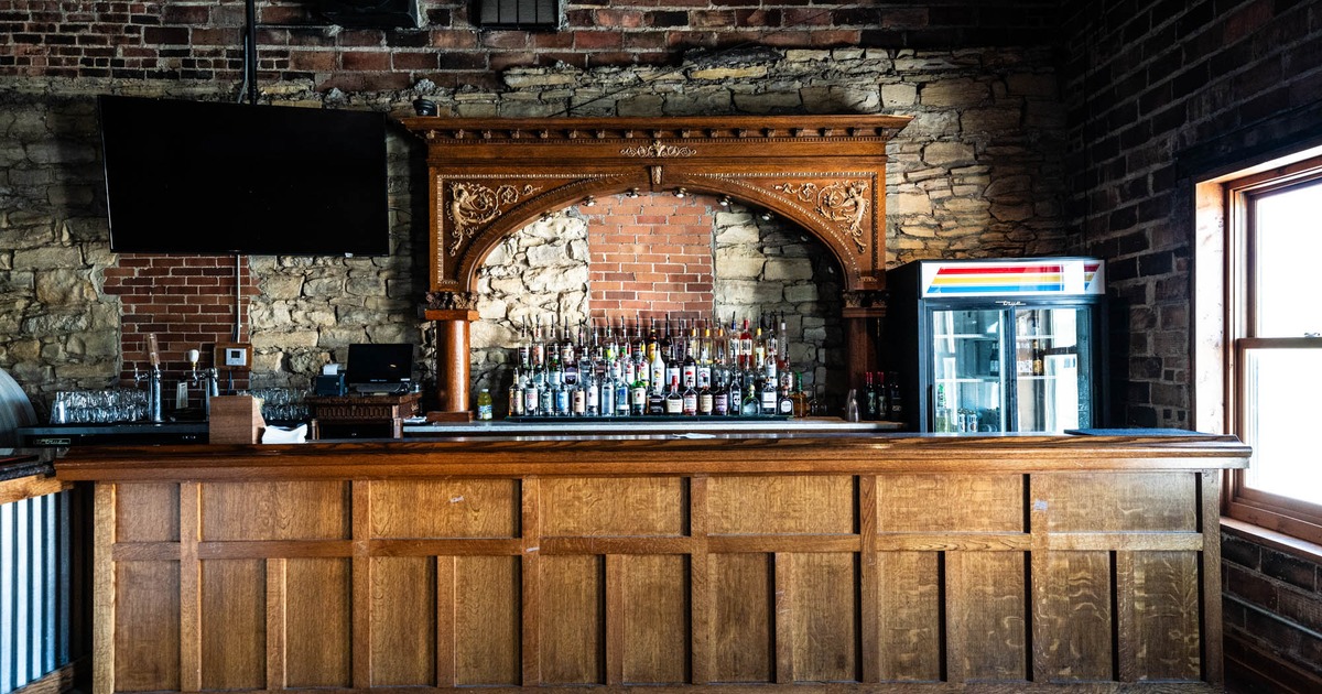 Wooden bar with a full liquor selection, brick and stone walls, and a TV