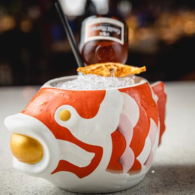 A cocktail served in a red and white fish shaped tiki mug, with crushed ice and dry citrus.