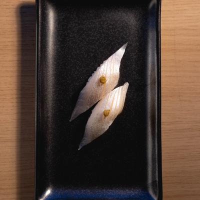 Two halibut nigiri pieces with citrus chili paste on a black rectangular plate.