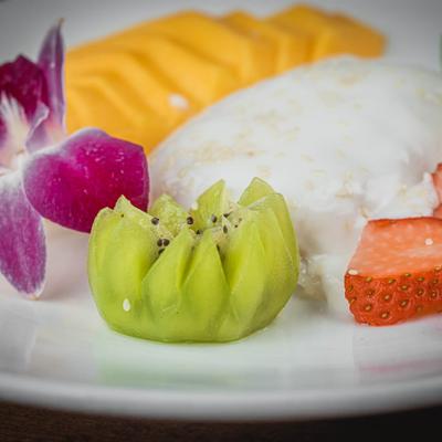 Sticky rice with mango, kiwi, strawberries and a purple flower garnish on the plate