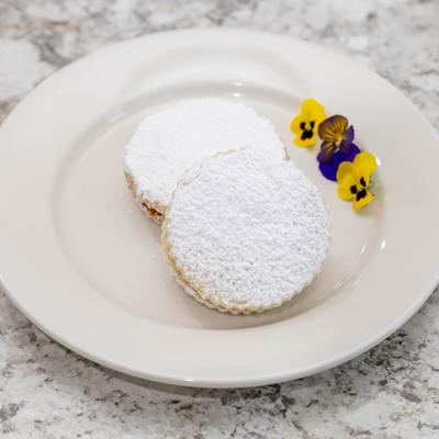 Alfajores arranged with colorful edible flowers on a white plate.
