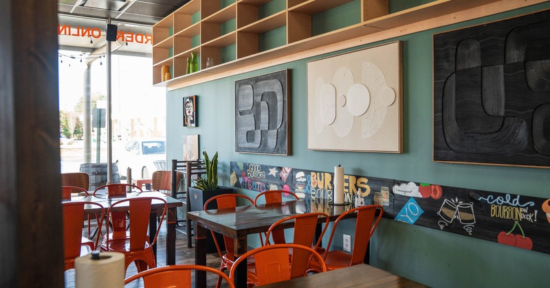 Interior with teal walls, abstract art, orange chairs and wooden tables.