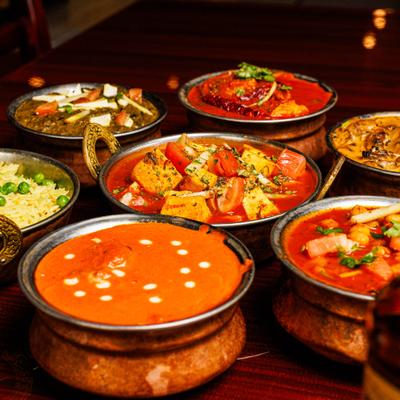 Indian curry dishes and basmati rice with green peas served in traditional copper bowls.