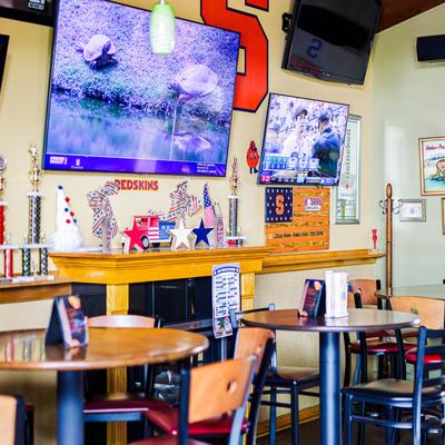 Tables and bar chairs in a room with TVs and sports decor on the walls.