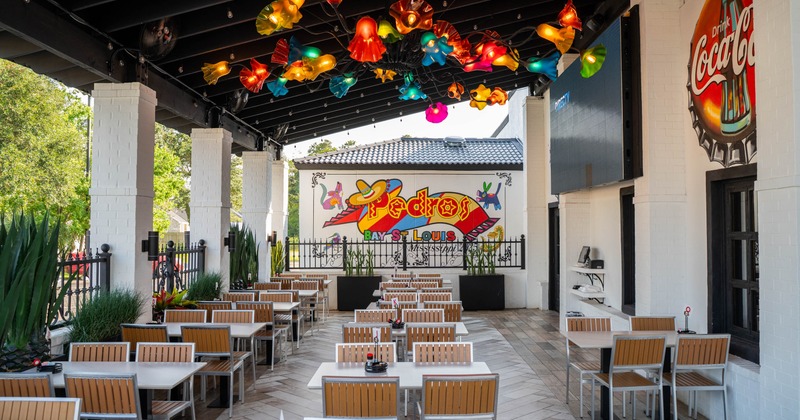 Outdoor dining area with colorful ceiling lights, tables with wood accents and murals