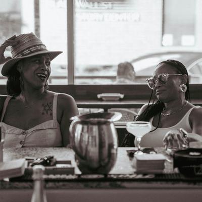 Two guests  sitting at a bar, share a laugh, drinks and bar items in front.