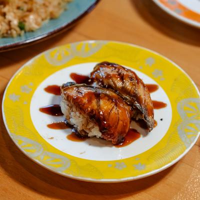 Glazed sushi pieces with sauce on yellow and white plate.