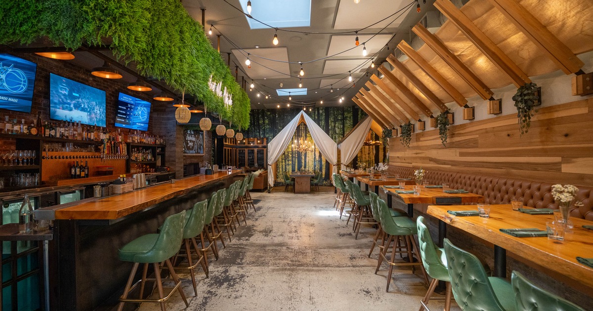 Cozy restaurant interior with wooden decor, green chairs, and hanging plants