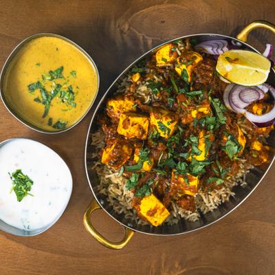 Paneer curry over spiced rice with raita and dal on the side.