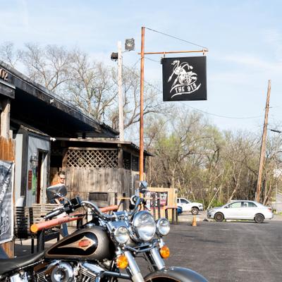 Motorcycle parked outside a bar with a hanging sign.