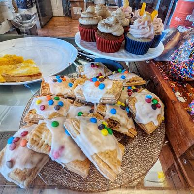 Glass display with assorted desserts including cupcakes, sprinkled doughnuts, and frosted hand pies.