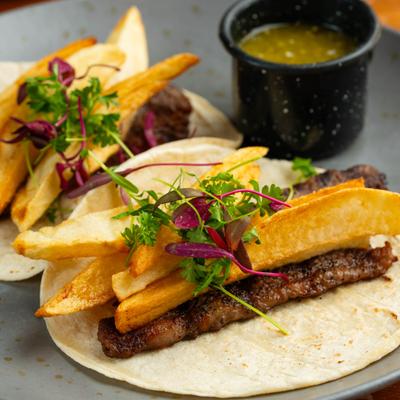 Steak and fries tacos topped with microgreens, served with green salsa..