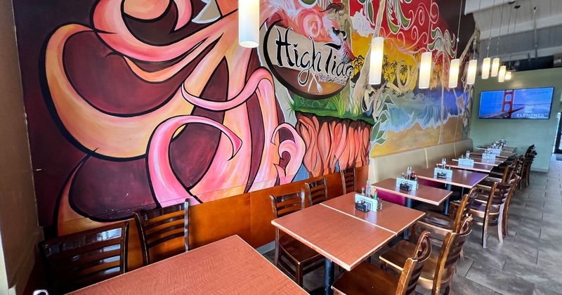 Interior dining area with wooden tables and chairs, a colorful mural on the wall