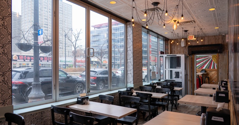 Interior, large windows, wooden tables, intricately patterned ceiling, and hanging light bulbs