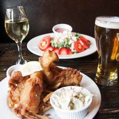 A plate of fish and chips, with a salad, a glass of white wine, and a pint of beer.