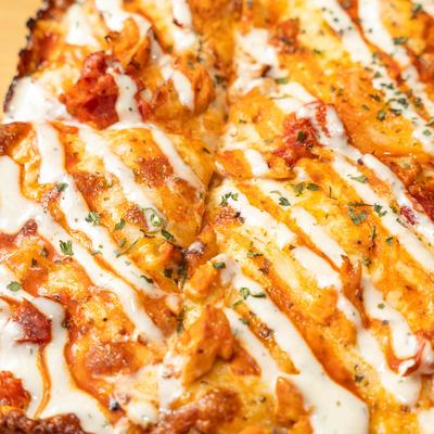 Close-up of a pizza with chicken, cheese, chilis, and ranch.