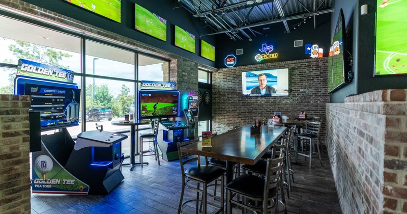 Inside, wooden table, arcade machines for golf, multiple flat-screen TVs showing sports events