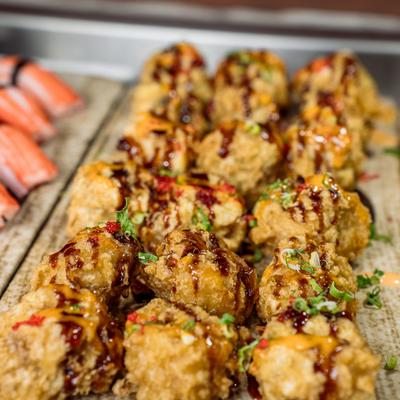 Fried sushi rolls drizzled with dark sauce, spicy mayo, and green onions.