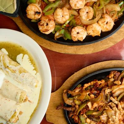 Shrimp fajitas, chicken fajitas, and enchiladas on a table.