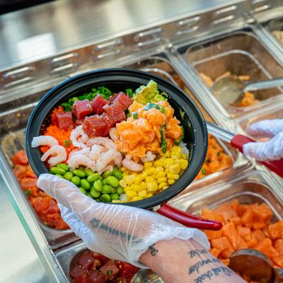 Gloved hand holding a poke bowl with tuna, shrimp, and vegetables.