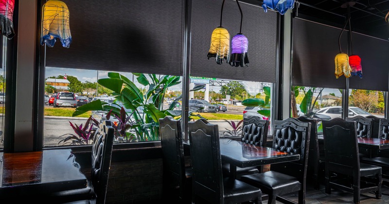 Restaurant interior with dark wood tables and tufted leather chairs by large windows