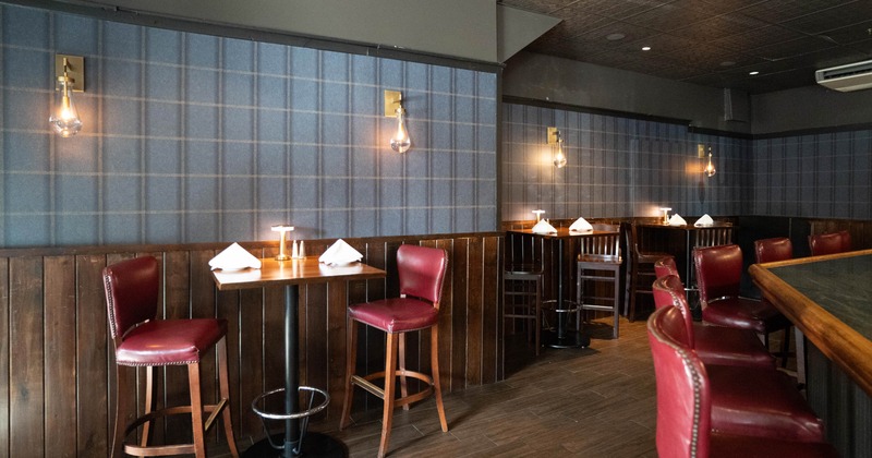 Interior of a restaurant with tables, red leather bar stools, wood-paneled walls